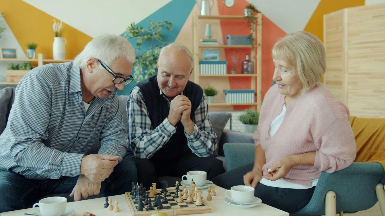 A group of cheerful seniors playing a game of chess and drinking tea in a bright, modern common area at a welcoming Thornhill retirement residence.
