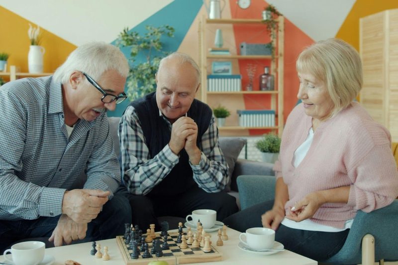 A group of cheerful seniors playing a game of chess and drinking tea in a bright, modern common area at a welcoming Thornhill retirement residence.